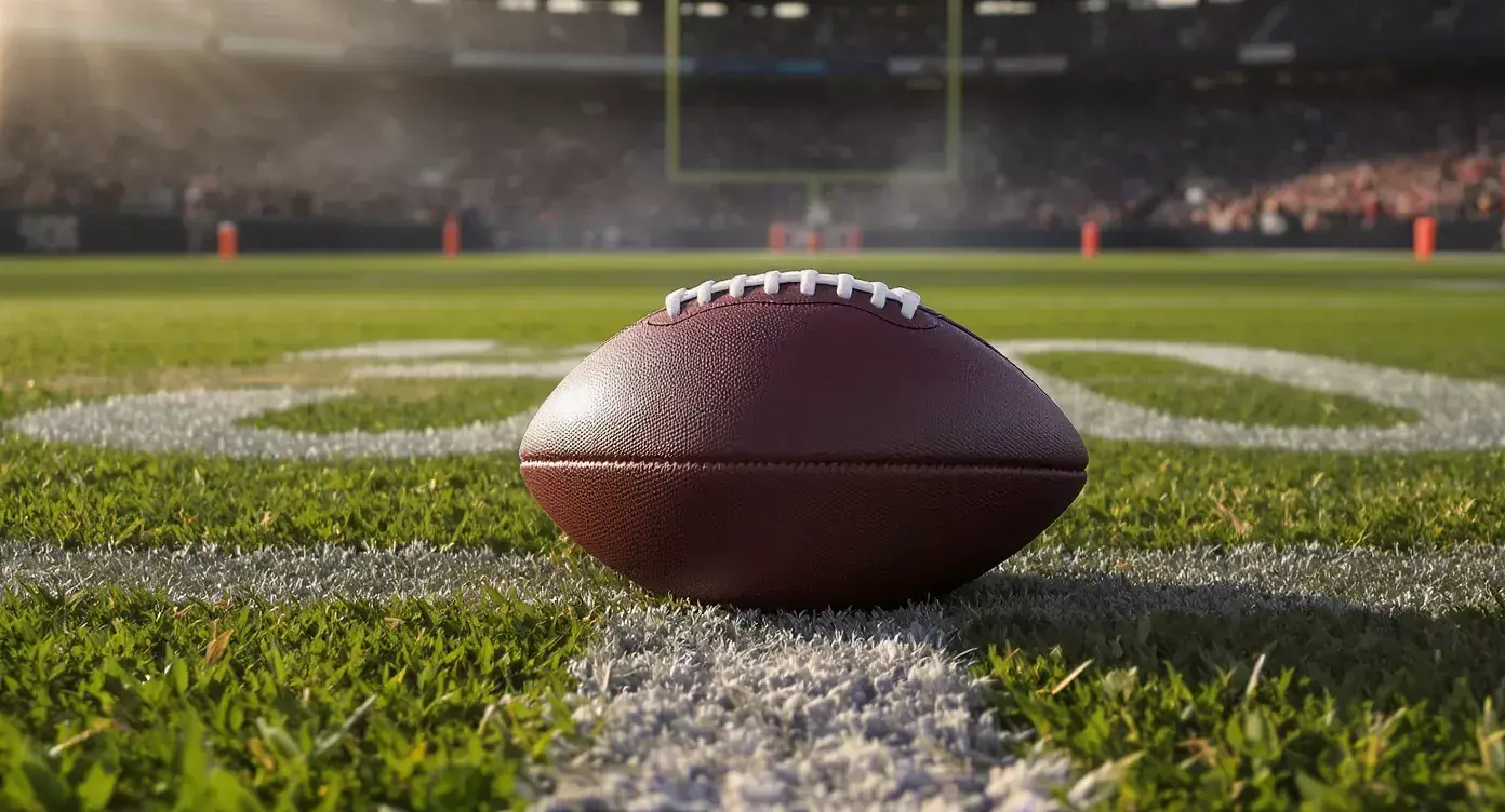 A leather American football resting on the painted yard-line markings of an NFL pitch at dusk